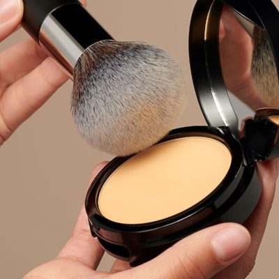 A fluffy brush applying powder foundation from a compact with a mirror.